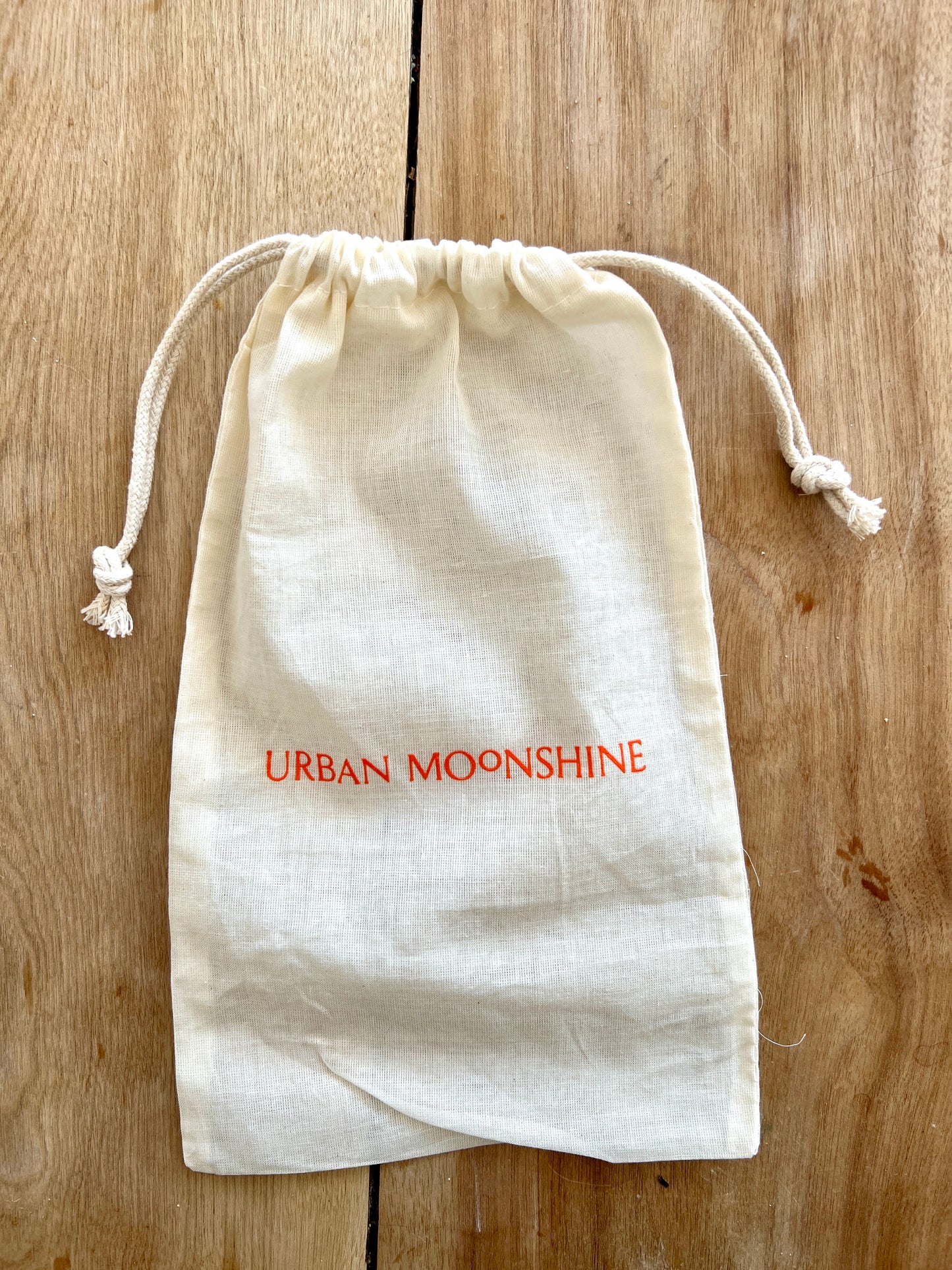 White drawstring bag with 'Urban Moonshine' text on a wooden surface